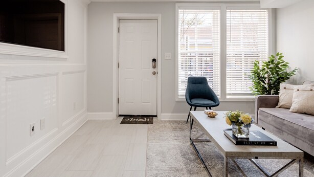 A modern living room with a white door, a blue chair, a white sofa, and a coffee table with a book and flowers. - Georgetown - 1-BR- Apt #1-450 SF (Near CAMPUS)  (Washington)