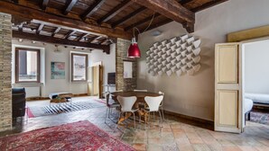 Une pièce spacieuse avec un plafond en bois, une table à manger ronde, des chaises blanches, un luminaire rouge suspendu et un tapis à motifs.