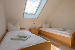 Quarto com duas camas, claraboia, mesa de cabeceira e criado-mudo.
