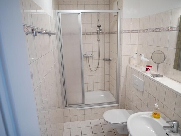 A bathroom with a glass-enclosed shower, a toilet, and a sink with a mirror and toiletries.