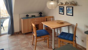 Una habitación pequeña con un escritorio de madera, dos sillas con cojines azules, una lámpara colgante y un estante con objetos decorativos.