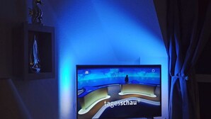 Un televisor montado en la pared con una luz azul ambiental, un caballito de mar decorativo y un cuadro enmarcado.