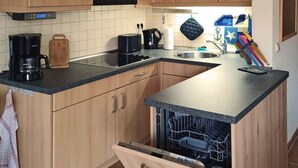 Cocina compacta con armarios de madera, microondas, cafetera y lavavajillas.
