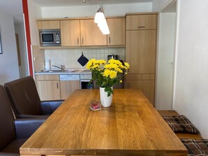 Une cuisine moderne avec des meubles en bois, un four à micro-ondes et une table à manger agrémentée d’un vase de fleurs jaunes.