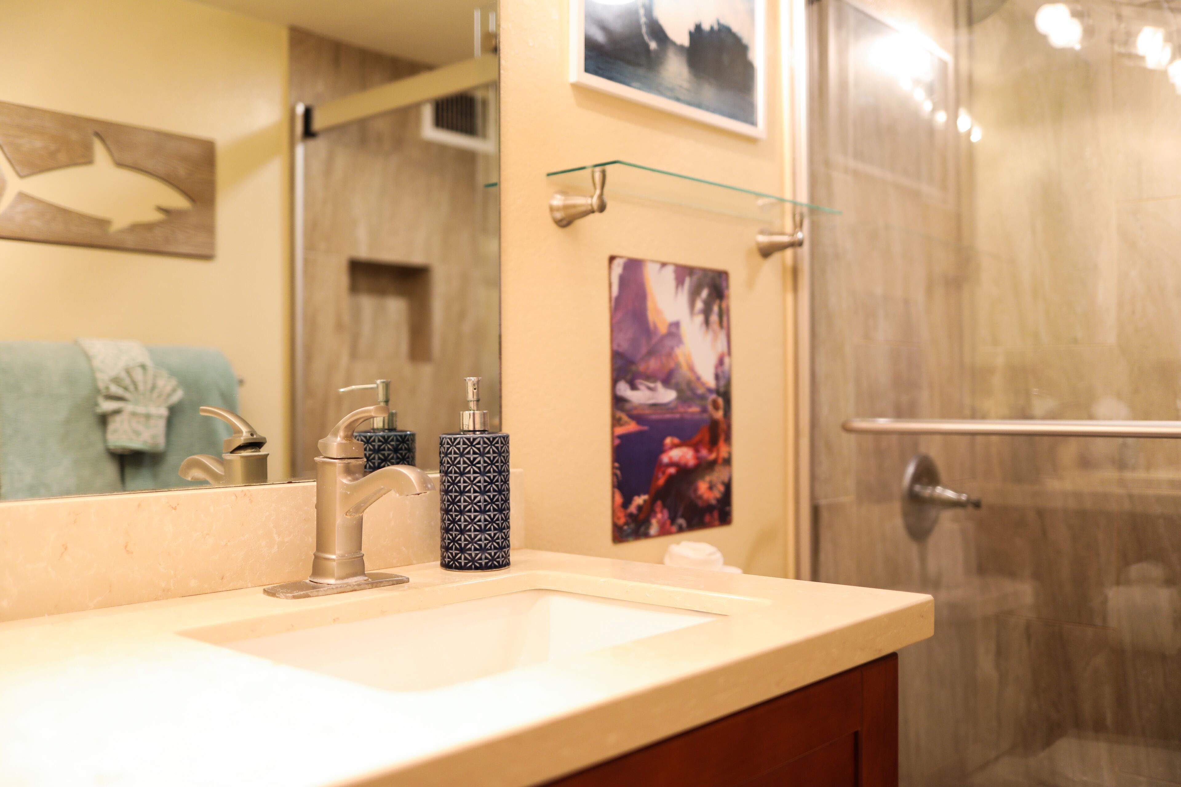A bathroom with a sink, faucet, and two patterned soap dispensers. A glass shower door is visible in the background.