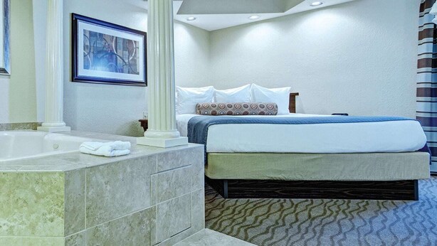 Une chambre d’hôtel avec une grande baignoire, un lit avec un matelas bleu et du linge de lit blanc, et deux œuvres d’art encadrées accrochées au mur.