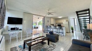 A spacious living room with a flat-screen TV, a coffee table, and a sofa. There is a kitchen area with a refrigerator and a dining table with chairs. - Serenity By the Beach, Private pool & El Yunque rainforest. 2BR. - 2 FULL BA. (Luquillo)