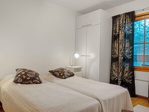 Une chambre avec deux lits, une table de chevet avec une lampe, une fenêtre avec des rideaux et une armoire.