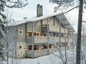Um edifício com vários andares e varanda em cada pavimento, rodeado por árvores cobertas de neve.
