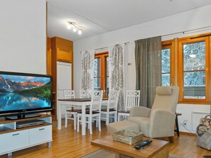 En stue med et fladskærms-tv, en sofa, et spisebord med stole og et vindue med gardiner.
