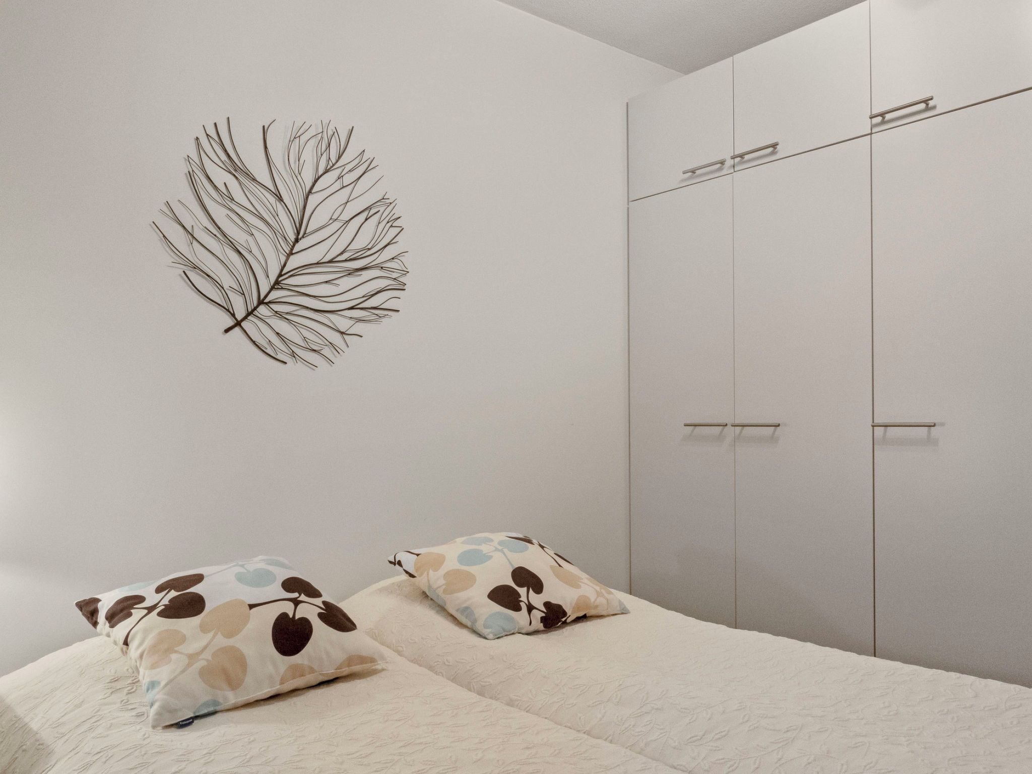 A bedroom with a bed, two pillows, a wall-mounted leaf decoration, and a wardrobe.