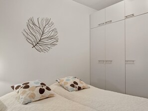 Quarto com cama, duas almofadas, um enfeite de folha na parede e um guarda-roupa.