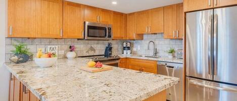 A modern kitchen with wooden cabinets, a granite countertop, stainless steel appliances, and a built-in oven.