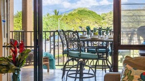 A dining area with a view of a green hill, a table set with plates and glasses, and a chair with a cushion.