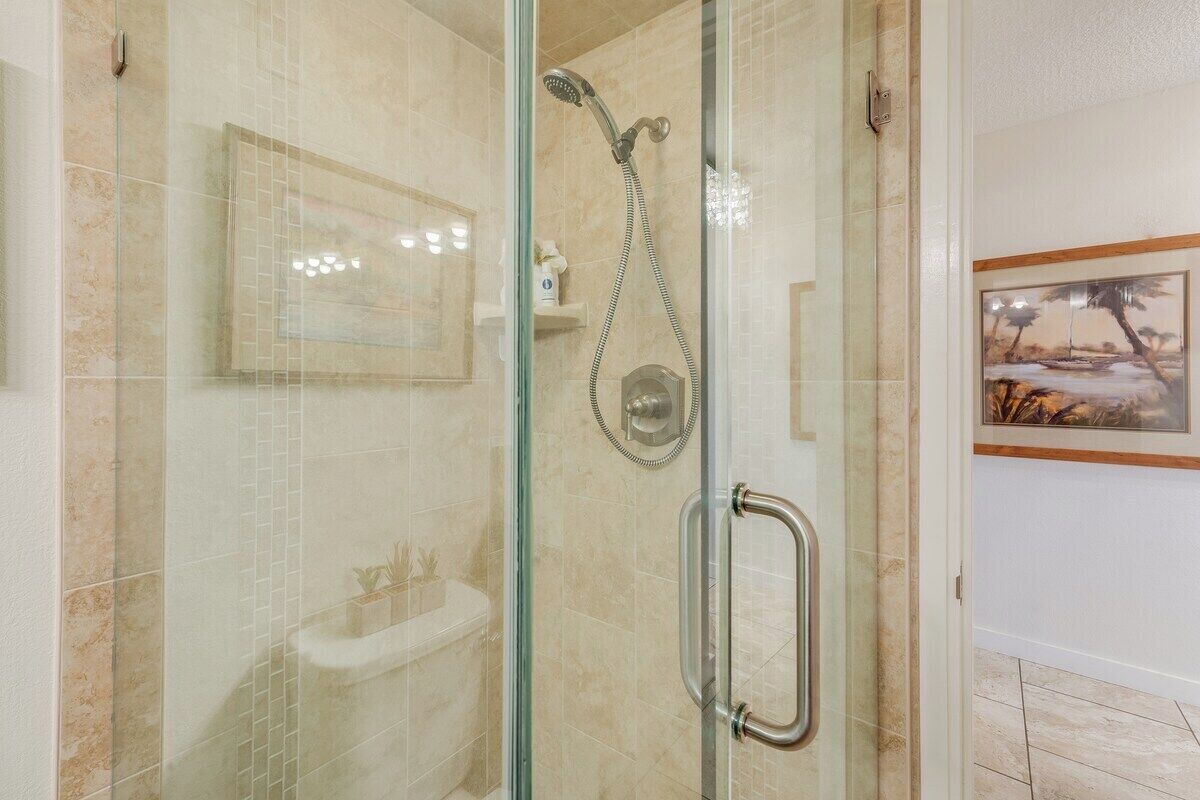 A glass-enclosed shower with a handheld showerhead, a glass door, and a wall-mounted sink.
