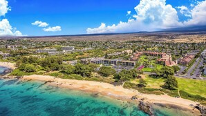 An aerial view of a coastal town with a beach, residential buildings, and clear blue waters.