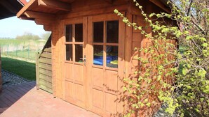 A wooden cabin with a sloped roof, a large window, and a door. - Kiek Wiet - Kiek Wiet: Vacation home for 6 people right on the water (Krummhörn)