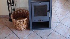 Una estufa de leña en una habitación con suelo de baldosas, una cesta de mimbre y una silla.