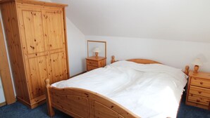 A bedroom with a wooden bed, a wardrobe, a bedside table with a lamp, and a mirror. - Kiek Wiet - Kiek Wiet: Vacation home for 6 people right on the water (Krummhörn)