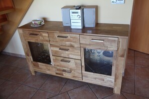 Een houten kast met glazen lades, een klein tafeltje met een kop en een afstandsbediening, en een speaker erbovenop.