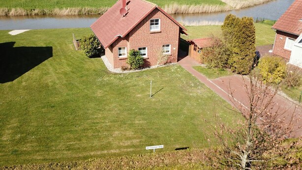 A single-story brick house with a red roof, a small front yard, and a sign indicating 'Ant Greeter Deep'. - Kiek Wiet - Kiek Wiet: Vacation home for 6 people right on the water (Krummhörn)