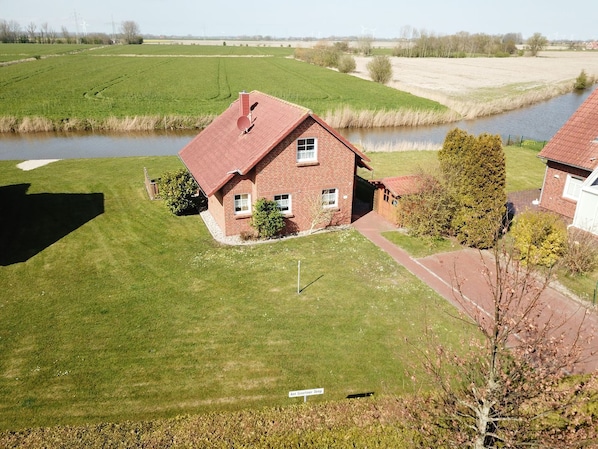 A single-story brick house with a red roof, a small front yard, and a sign indicating 'Ant Greeter Deep'. - Kiek Wiet - Kiek Wiet: Vacation home for 6 people right on the water (Krummhörn)