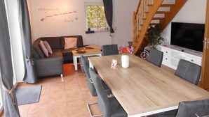 A modern living room with a wooden dining table, grey sofas, and a staircase. - Friesenhuske - Great vacation home (85sqm) for 5 people with garden in Norden (Norden)