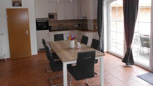 A modern kitchen with white cabinets, a wooden dining table, and black chairs. - Friesenhuske - Great vacation home (85sqm) for 5 people with garden in Norden (Norden)