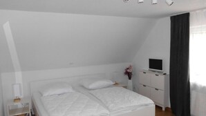 A bedroom with a white bed, a TV on a dresser, and a nightstand with a lamp. - Friesenhuske - Great vacation home (85sqm) for 5 people with garden in Norden (Norden)