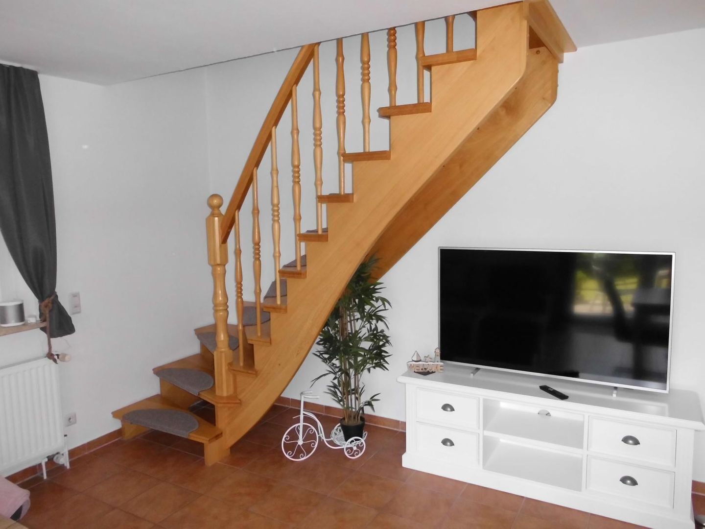 A wooden staircase leading to a landing with a flat-screen TV on a white cabinet.