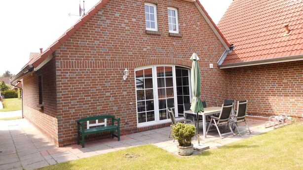 A brick house with a tiled roof, a patio with outdoor furniture, and a green bench. - Friesenhuske - Great vacation home (85sqm) for 5 people with garden in Norden (Norden)
