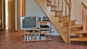A living room with a wooden staircase, a television, and a bookshelf. - Friesenstern - Holiday home (100sqm) for 6 persons with garden in a quiet location of (Norden)