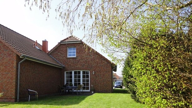 A brick house with a tiled roof, a front door, and a small patio area with a table and chairs. - Friesenstern - Holiday home (100sqm) for 6 persons with garden in a quiet location of (Norden)