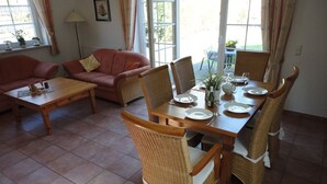 A dining area with a wooden table set for four, surrounded by wicker chairs. - Friesenstern - Holiday home (100sqm) for 6 persons with garden in a quiet location of (Norden)