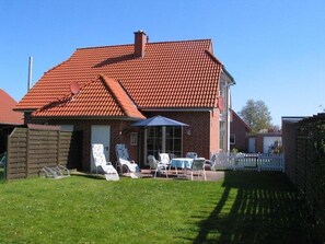 Uma casa com telhado de telhas vermelhas, um alpendre com móveis de exterior e uma cerca branca de piquete.