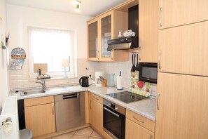 A compact kitchen with wooden cabinets, a built-in oven, a microwave, and a dishwasher.