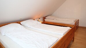 Une petite pièce unique comprenant deux lits superposés en bois, une table de chevet et une lampe.