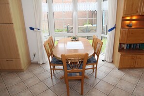 Uma área de refeições com uma mesa de madeira redonda, seis cadeiras e uma janela com cortinas.