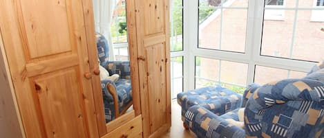 Habitación con armario de madera, una silla azul estampada y un ventanal con vistas a un edificio de ladrillo y follaje.