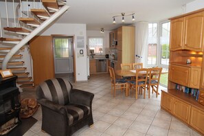 A cozy living room with a fireplace, a dining area with wooden furniture, and a kitchen with a refrigerator and stove.