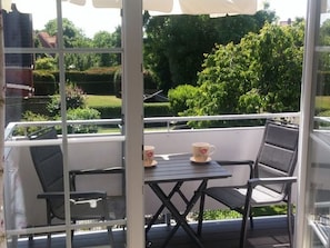 Ein Balkon mit Tisch und Stühlen, der auf einen Garten mit Bäumen und einer Hecke blickt.