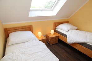 Un dormitorio con dos camas, tragaluz, cabeceros de madera, mesitas de noche con lámparas y suelo de madera.