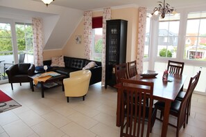 Ein Wohnzimmer mit einer Couch, Sesseln, einem Esstisch und einem Schrank.