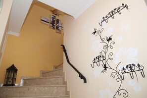 A staircase with a decorative wall on the right side featuring floral patterns and a black metal handrail. - Dornröschen - Ferienwohnung mit Direktem Wasserblick (Krummhörn)