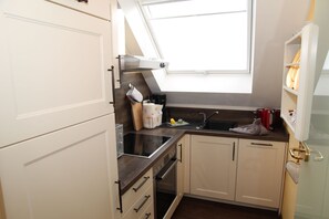 Eine kleine Küche mit weißen Schränken, einer schwarzen Arbeitsplatte, einem Fenster über der Spüle und einem kleinen Backofen.