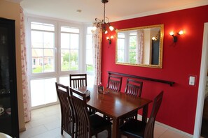 A dining area with a red wall, a large window, and a chandelier.