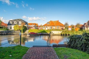 A canal with a boat docked, surrounded by houses with red roofs and a grassy area with a brick pathway.
