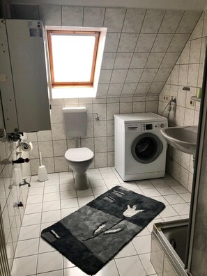 Een kleine badkamer met toilet, wasmachine, wastafel en een klein raam.
