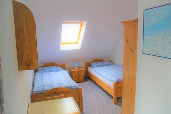 A small, single-room accommodation with two wooden beds, a small table, a nightstand, and a skylight. - Flüthörn - Cozy semi-detached house with unobstructed views (Norden)