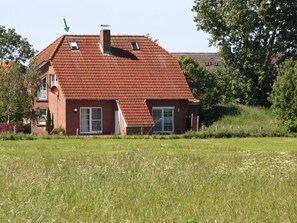 A two-story house with a red-tiled roof, a chimney, and a small window on the upper floor. - Flüthörn - Cozy semi-detached house with unobstructed views (Norden)